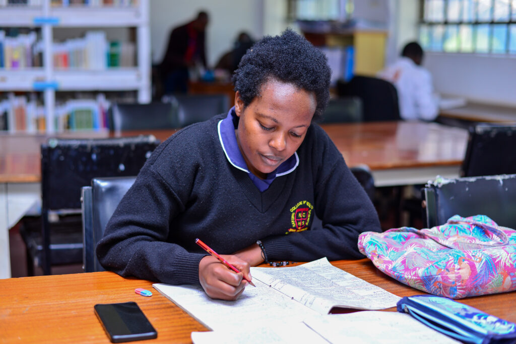Students studying in the college library surrounded by bookshelves, study desks, and academic resources in a quiet learning environment.